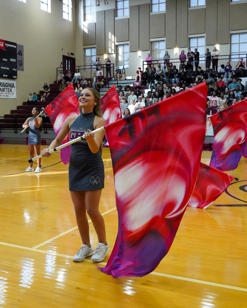 A color guard member spins a flag during a school pep rally in a gymnasium.