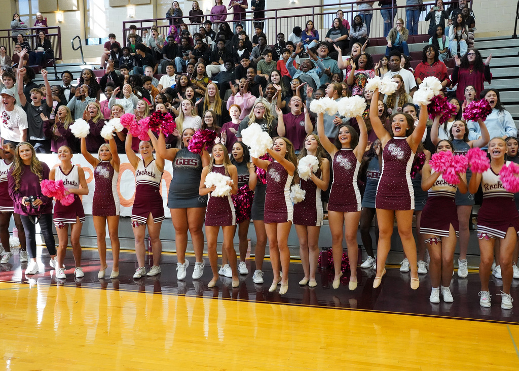 Students wearing Gardendale High School auxiliary and cheer uniforms smile and cheer during a pep rally in the school gym.