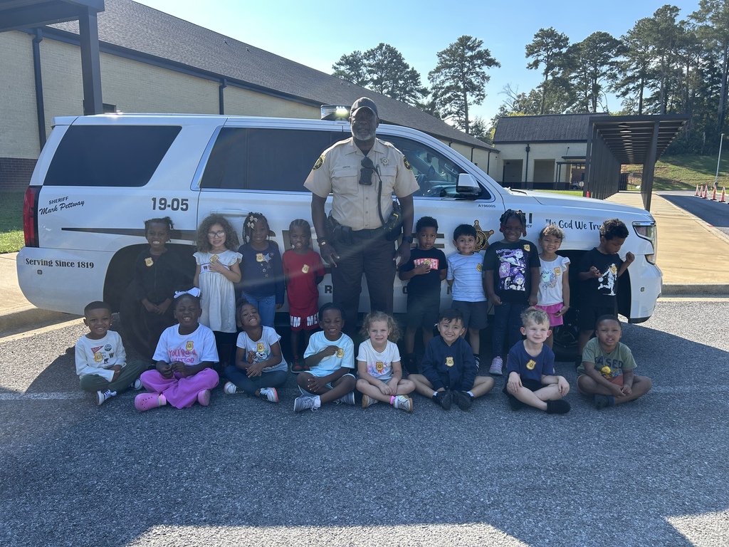 a group of students standing with our SRO by his police car smiling for a picture