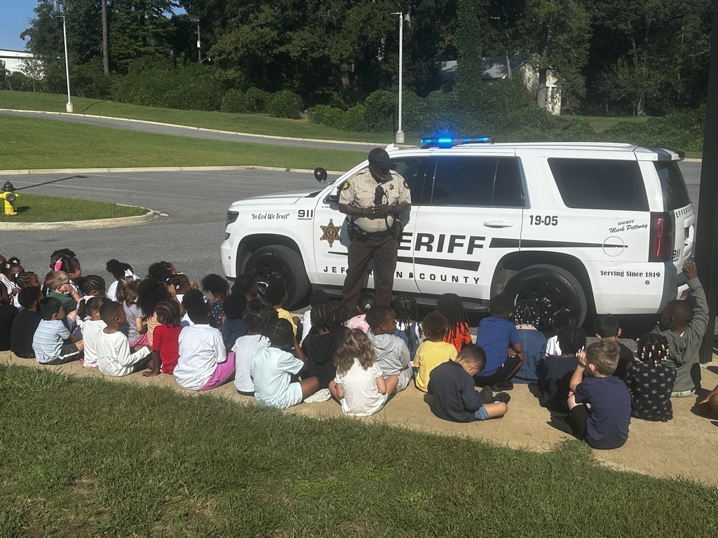 students sitting on the sidewalk listening to Officer Gregg talk to them