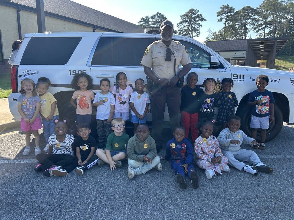 a group of students standing with our SRO by his police car smiling for a picture