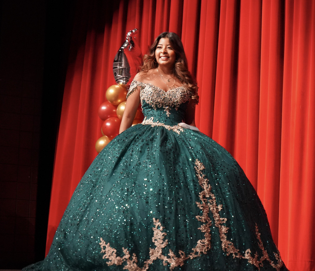 A student wearing a quinceañera walks across a stage.