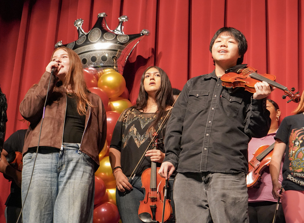 Students sing and play instruments during a performance on a stage.