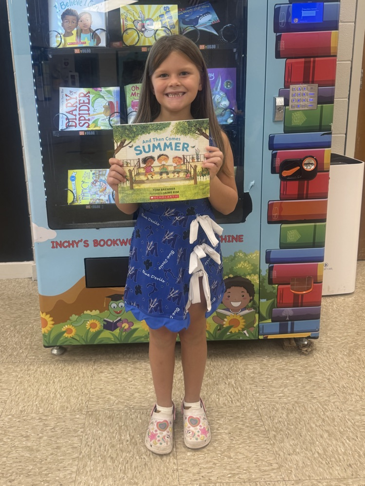 Young girl in blue dress, smiling, and holding a book