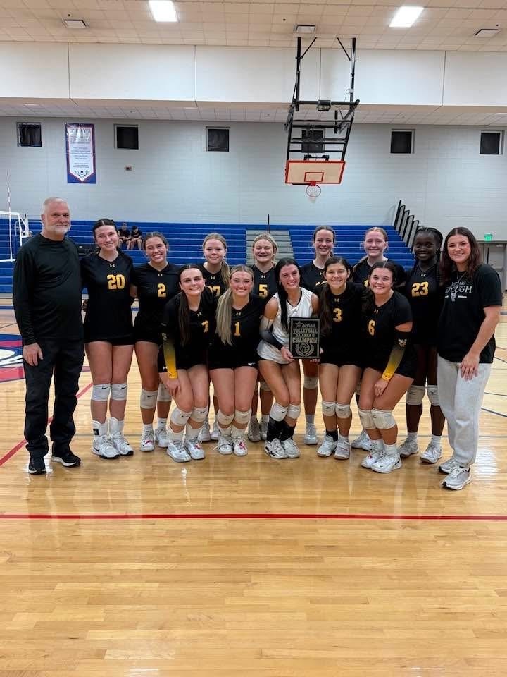 Corner High School volleyball players and coaches stand together in a school gym and pose for a photo.