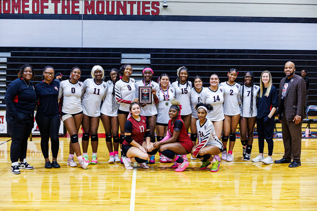 Shades Valley's principal, volleyball team, and volleyball coaches pose for a photo inside a school gym.