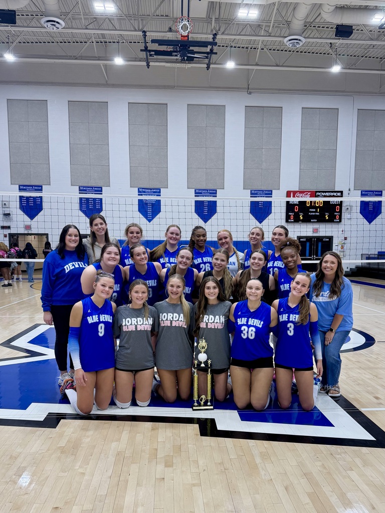 Mortimer Jordan volleyball players pose for a photo with a trophy inside a school gym.