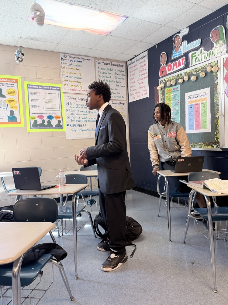 Two students presenting. one in a black suit and one in a tan jacket