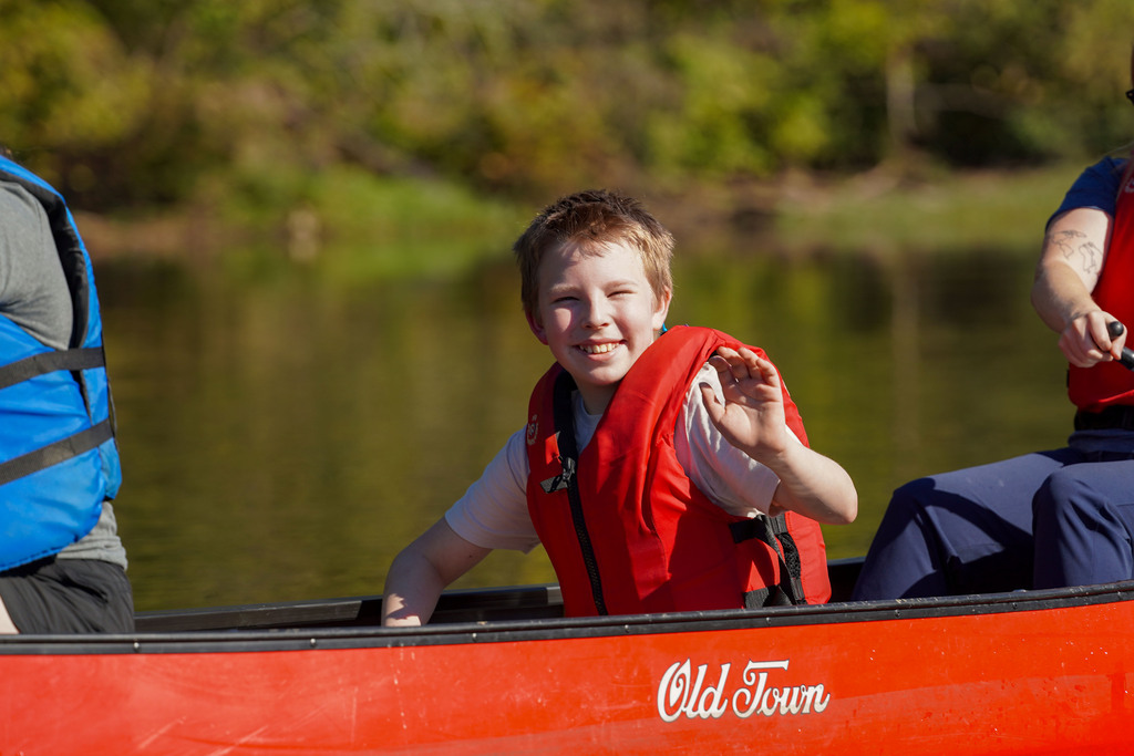 A child waves while sitting in a canoe on a lake.