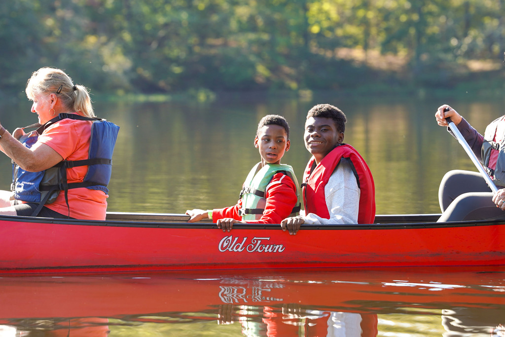 Two children sit in a canoe being paddled by two women.