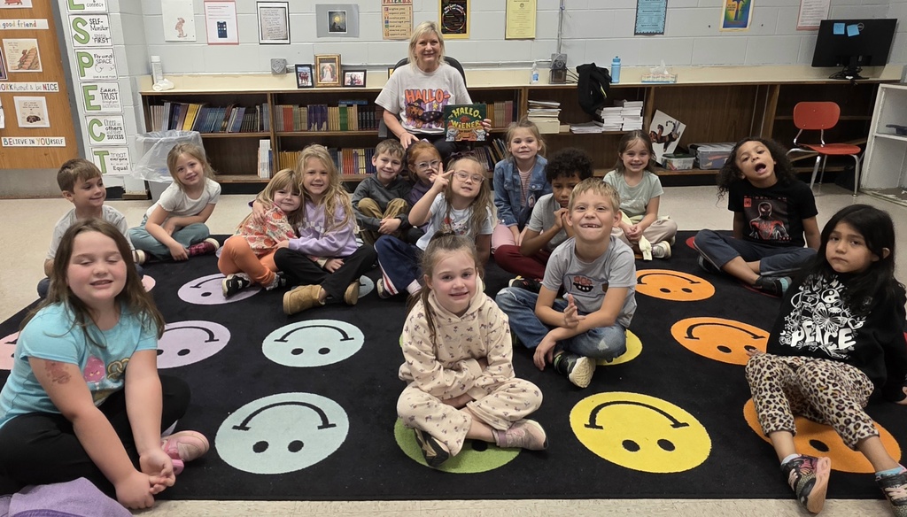 Teacher holding a book and students sitting in front of her on the rug
