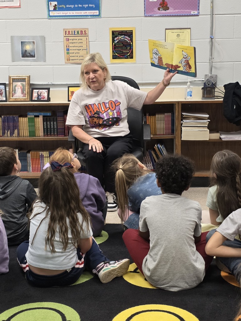A teacher holding up a book reading to students sitting on a rug