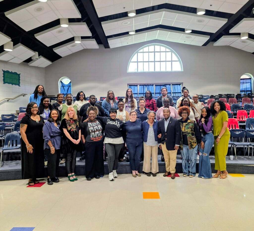 Educators stand together for a photo with leadership from the John F. Kennedy Center for the Performing Arts and a teaching artist in a choir room.