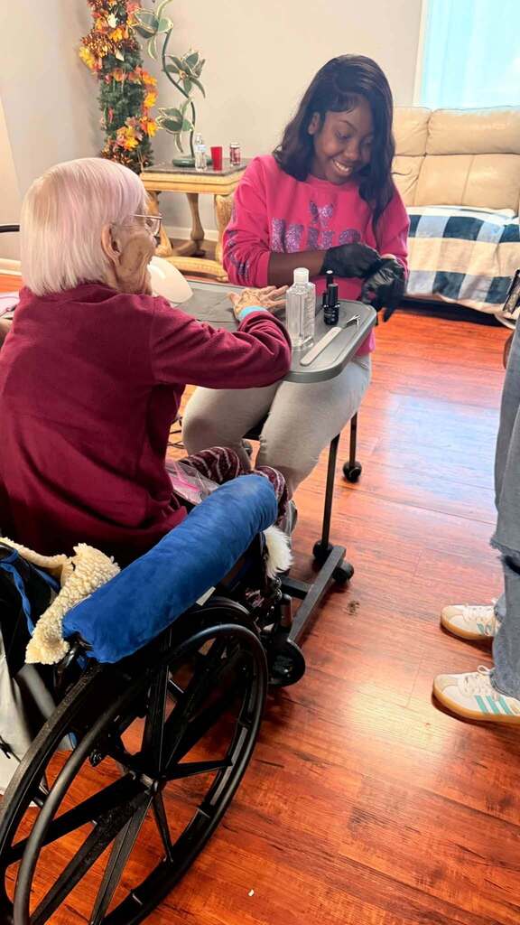 A student smiles while giving a woman a manicure.