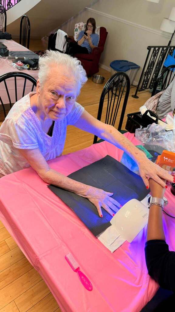 A woman sits at a chair and receives a manicure.