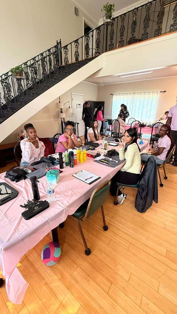 Students sit at a table with cosmetology supplies on it.