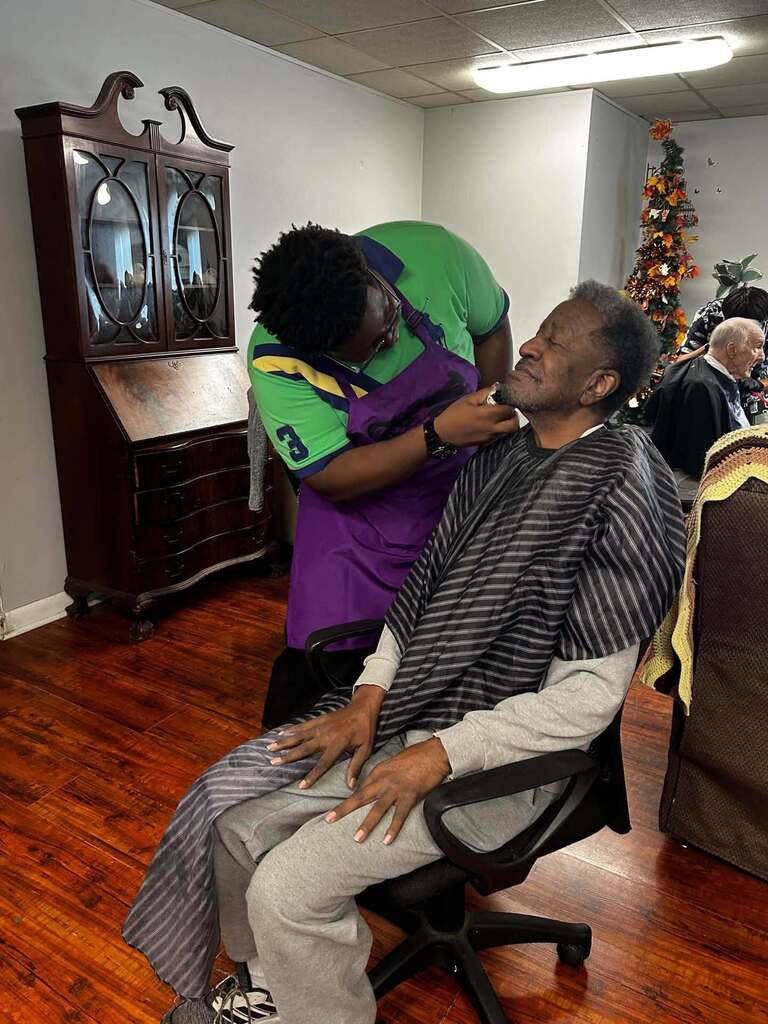 A student trims a man's beard.
