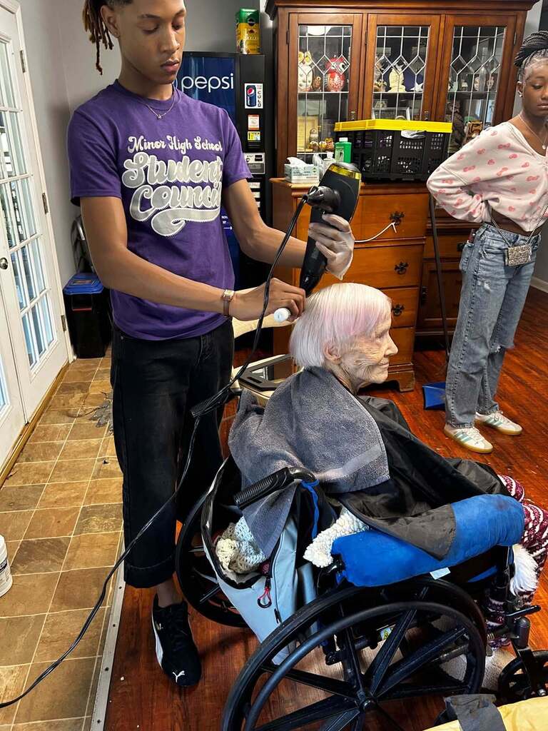 A student blowdries a woman's hair.