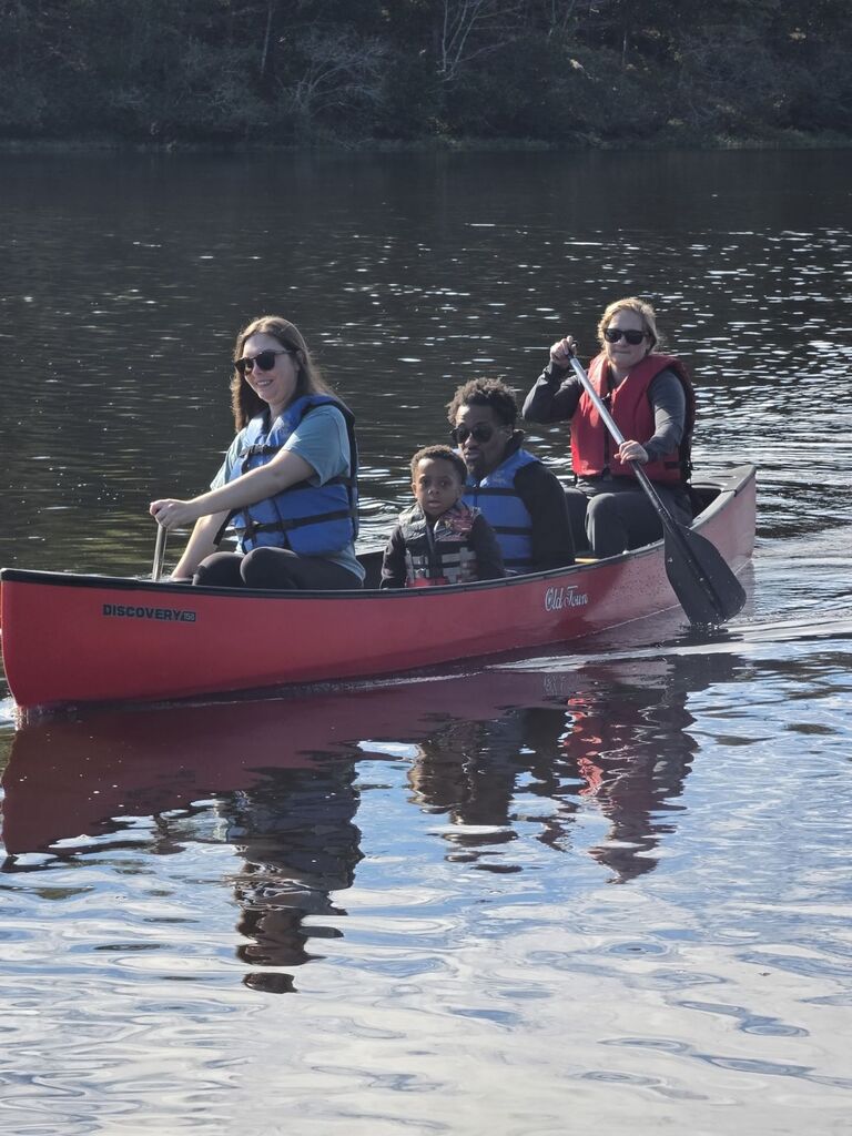 2 people sitting in the middle of a canoe while 2 others paddle the canoe