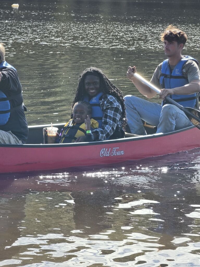 A mom and son smiling at the camera sitting in the middle of a canoe on the lake