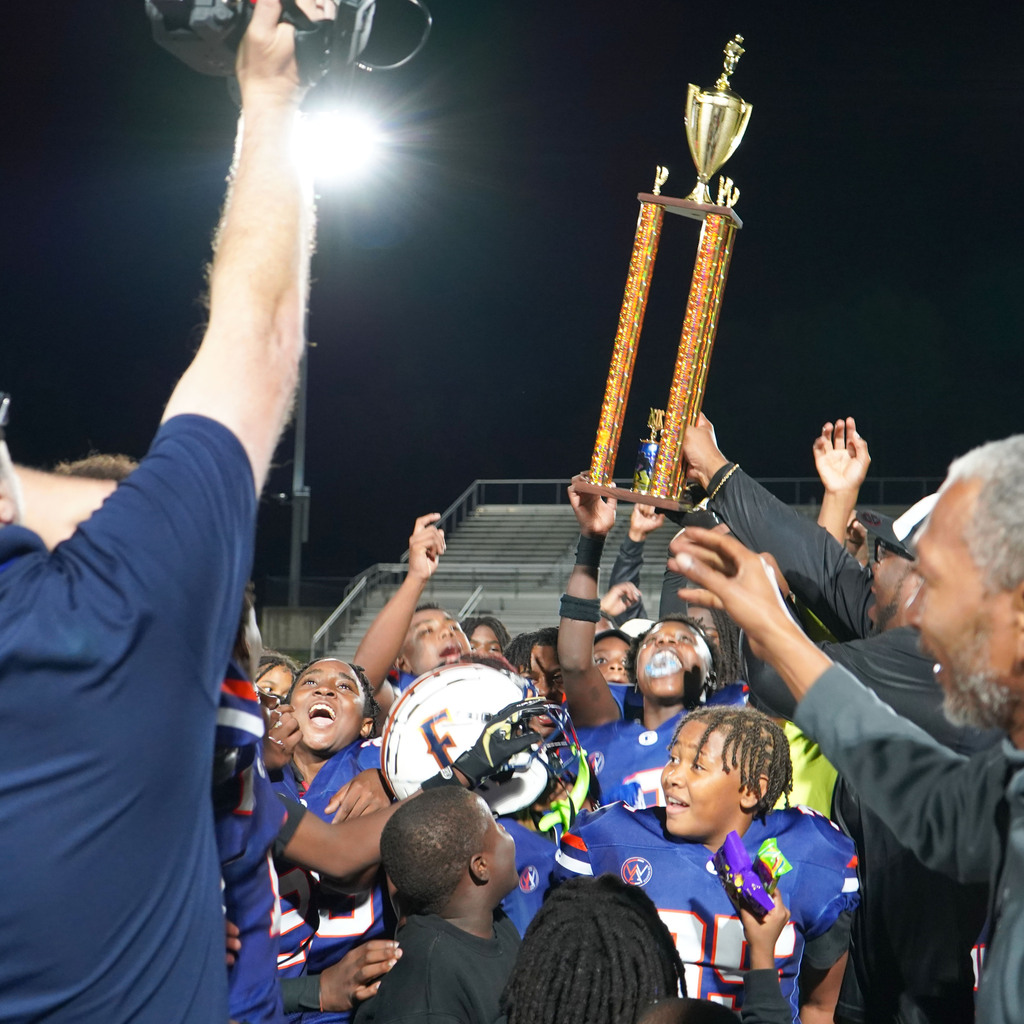 Fultondale football players hold up a trophy and celebrate on a football field.