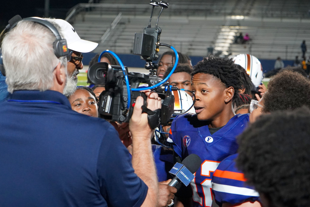 A football player speaks into a microphone during. a post-game interview on a football field.