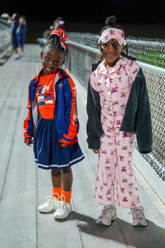 Two young girls stand in the bleachers of a football stadium and smile for a photo.