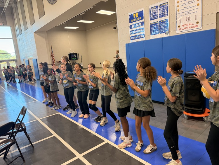 girls newcomb team standing by the stage in the gym watching their teammates run in for the opening of the newcomb game 
