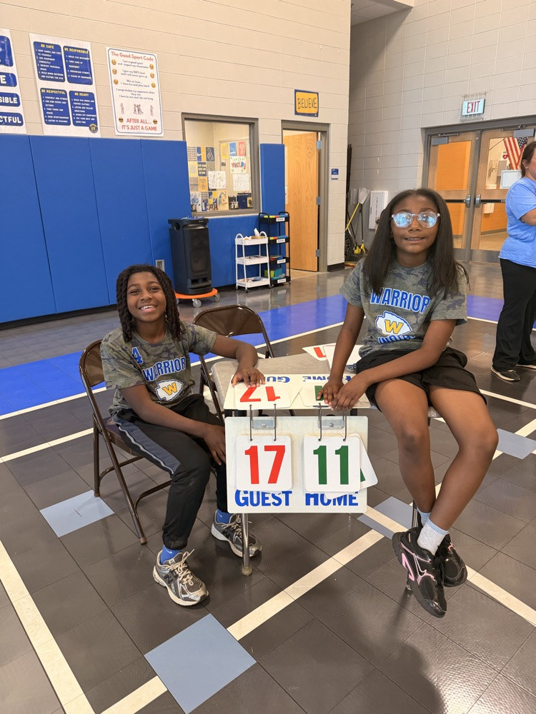 a girl sitting on the table and a boy sitting in a chair next to the table keeping score for the game 