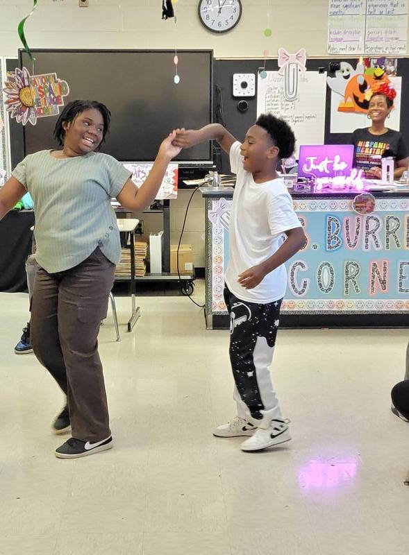 Two people dance together in a school classroom.