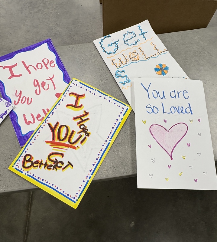 Four hand-decorated cards sit on a table. They read "I hope you get well", "I hope you get better", "Get Well Soon" and "You Are So Loved"