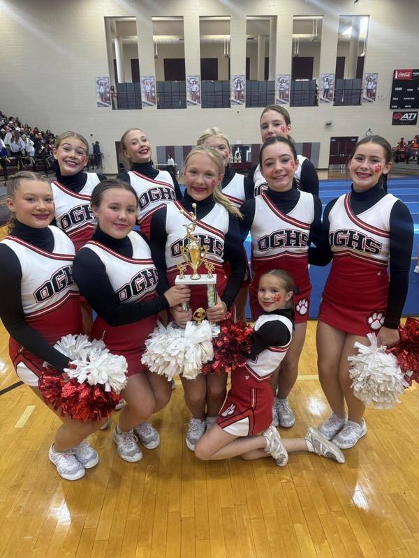 Oak Grove cheerleaders pose for a photo with a trophy while standing in a gym.