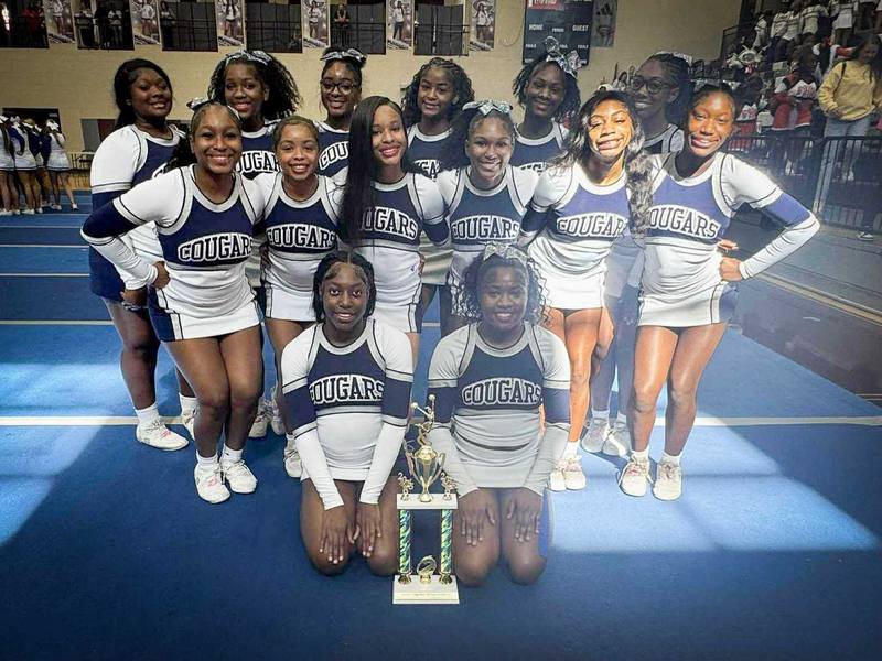 Clay-Chalkville cheerleaders stand and sit while posing with a trophy in a school gym.