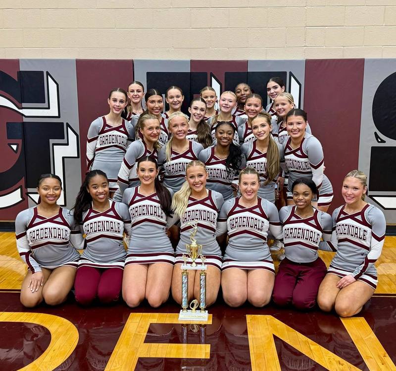 Gardendale High School cheerleaders pose with a trophy while sitting and standing in the high school's gym.
