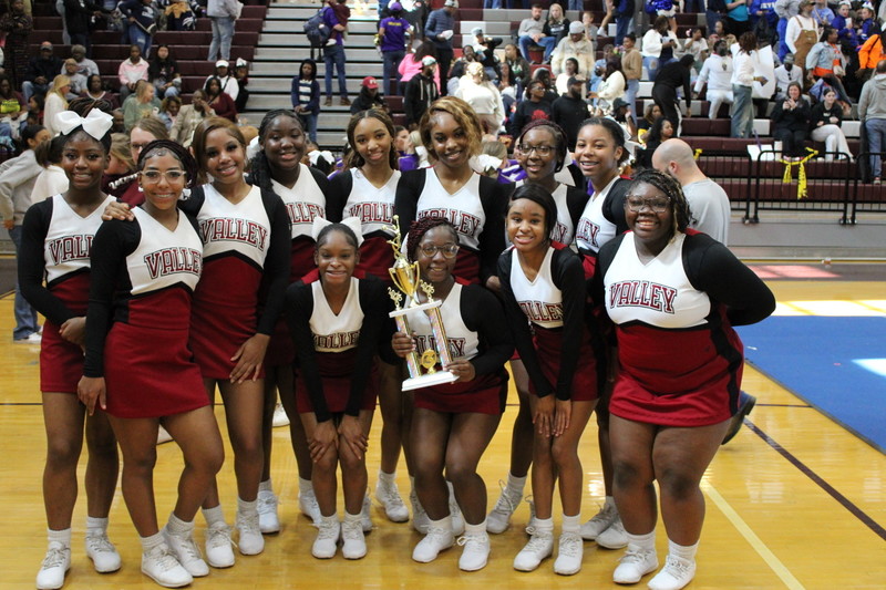 Shades Valley cheerleaders pose with a trophy while standing inside a school gym.
