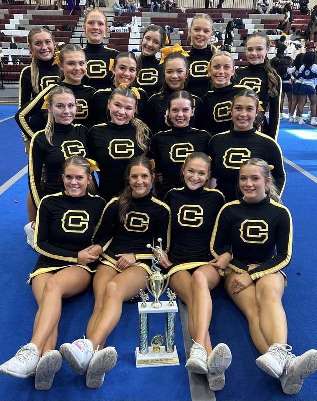 Corner High School cheerleaders pose for a photo while sitting and standing inside a school gym.