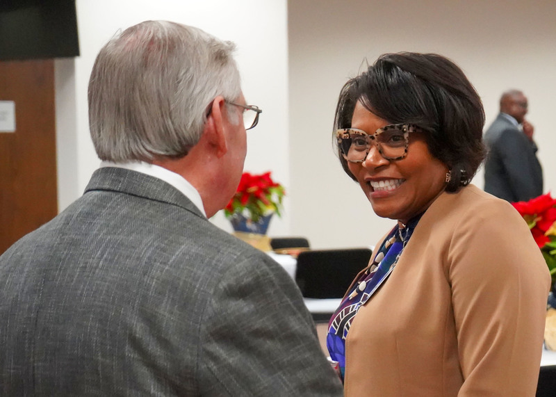 A man and a woman are having a discussion. The man is turned away from the camera and the woman is turned towards the camera, smiling. 