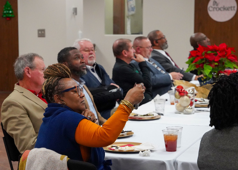 A group of men and women are sitting around a table during a mayors luncheon with Jefferson County Schools. The woman in the front of the picture is taking a picture with her cell phone. 