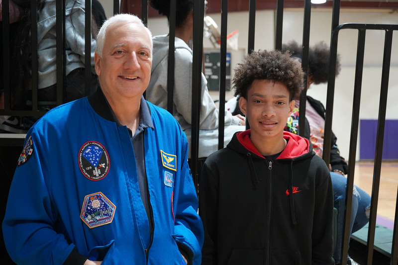 Former NASA Astronaut Mike Massimino stands with a Minor Middle School student for a photo inside a school gym. They both smile.