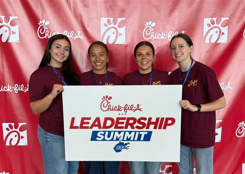 JHS Leadership Academy students holding up a sign for the Leadership Summit in front of a Chik-Fil-A step and repeat backdrop