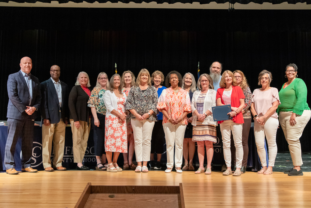 Several JCS retirees pose on stage with members of the BOE at a board meeting