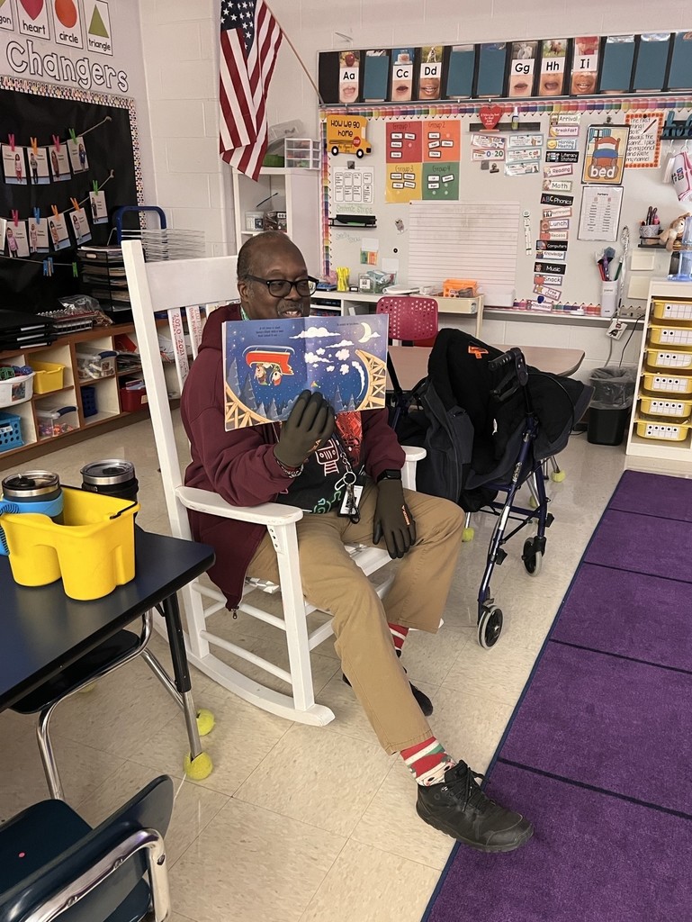 A man sits in a rocking chair reading a book aloud