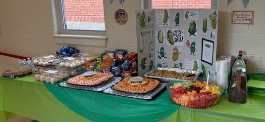 PTO Big Dill Display with lunch food including shrimp, snack bags, various types of pickles, fruit, pasta salad, cookies, cupcakes and drinks