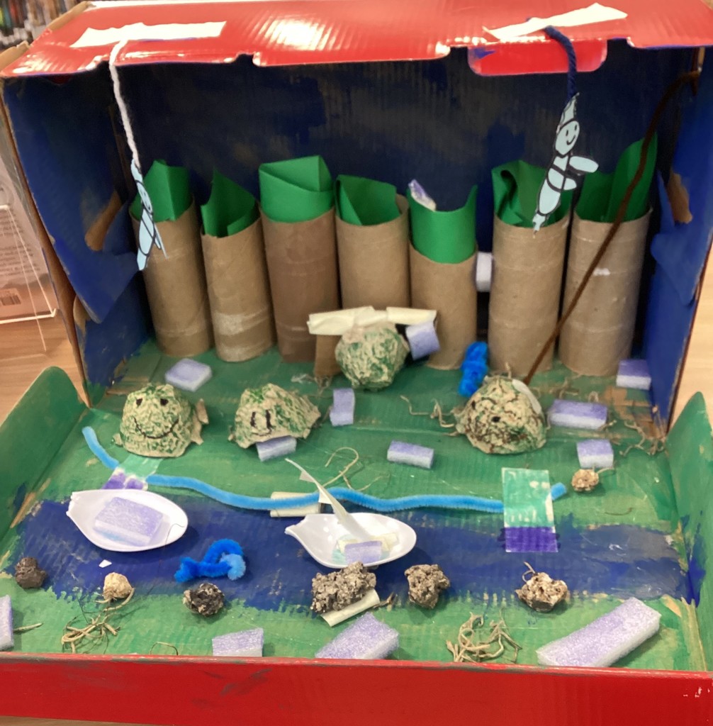 A box with blue paint, green paint, toilet paper rolls, and green paper for a river and forest habitat