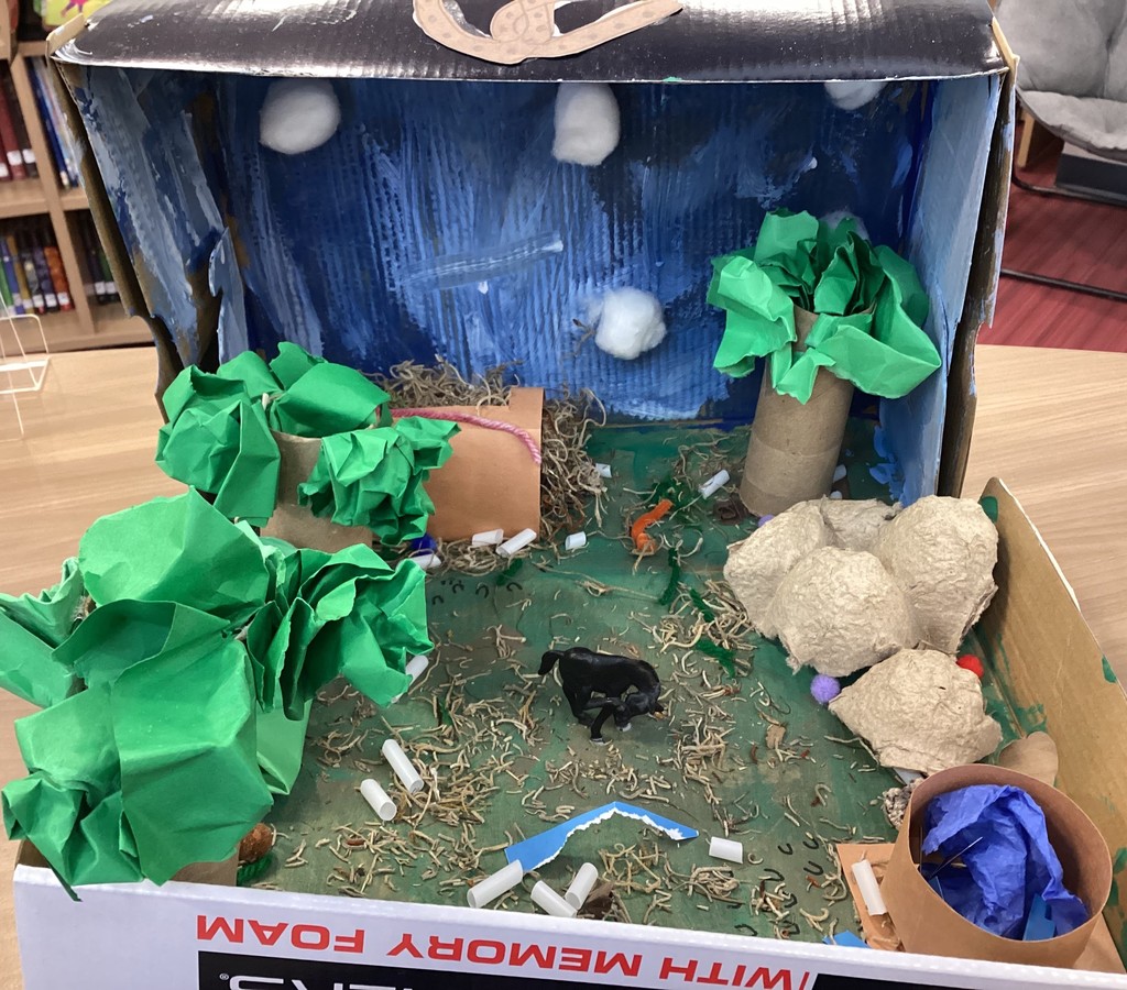 A box with green paint and moss for grass, toilet paper rolls and green paper for trees. It also has a plastic horse in the middle.