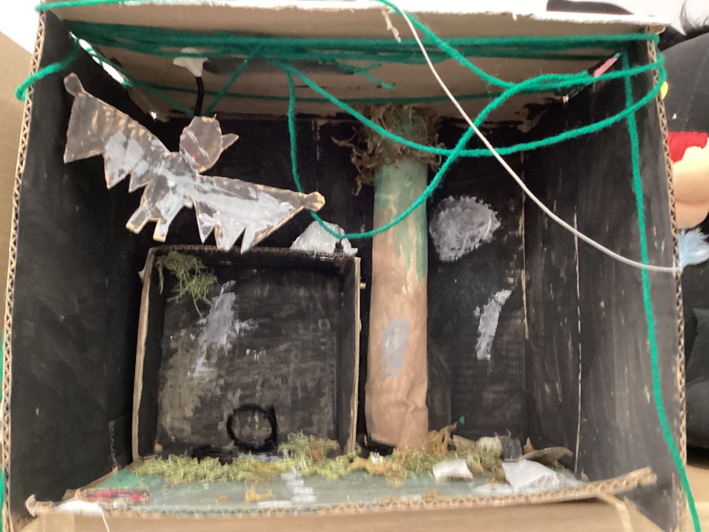 A box with black paint, green string, and moss for a forest habitat