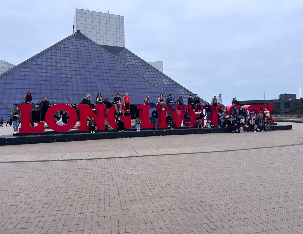 Students sitting on the "Long Live Rock" sign in front of the Rock and Roll HOF