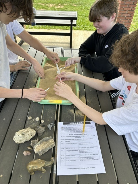 Students digging in the sand to look for rocks