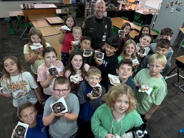 Students holding donuts and posing with Deputy