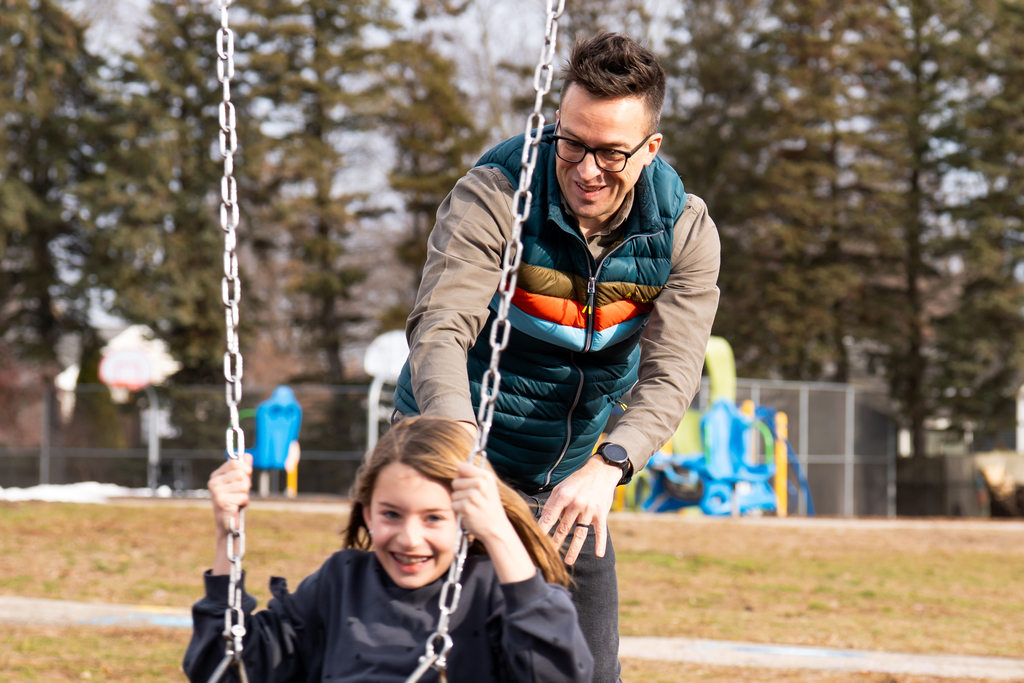 Watch Dog dad smiling and pushing daughter on swings